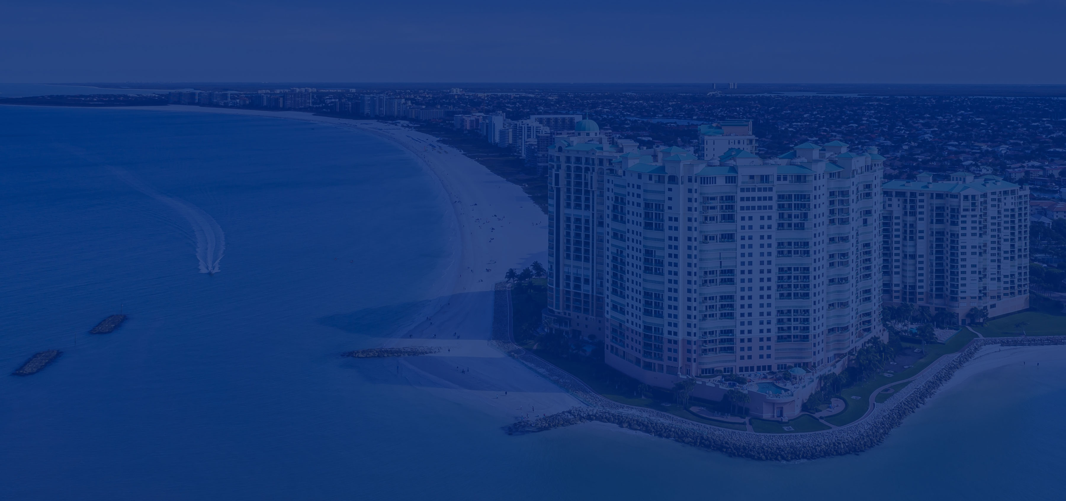 Aerial view of a curved beach and high-rise apartment buildings at dusk.